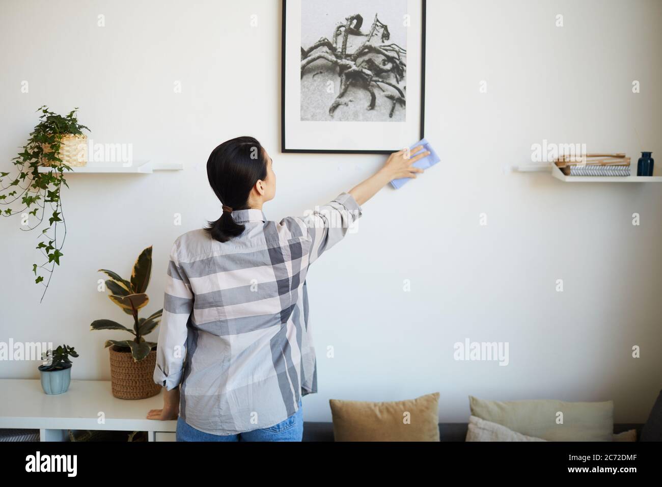 Rückansicht der jungen Frau, die Hausarbeit im Zimmer sie wischte den Staub mit Lappen aus dem Bild Stockfoto