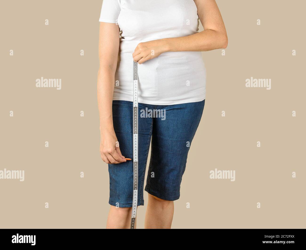 Kaukasische reife Frau in einem weißen T-Shirt und einer blauen Denim Capris gekleidet wird, um sie zu verkürzen und die Länge mit einem Maßband zu messen. Stockfoto