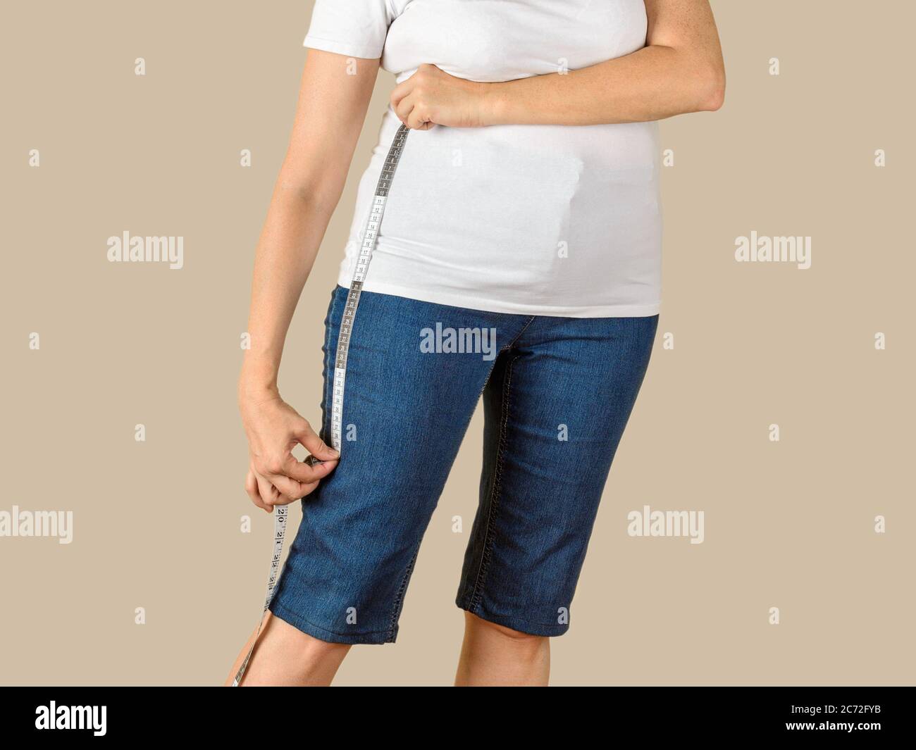 Kaukasische reife Erwachsene Frau in einem weißen T-Shirt und einer blauen Denim Capris gekleidet wird, um sie zu verkürzen und eine Schnittlinie auf der gewünschten Länge zu ziehen. Stockfoto