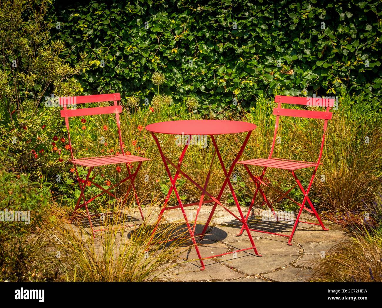 Bistrotisch aus rotem Metall mit zwei Stühlen auf einer runden Terrasse aus Stein. Stockfoto