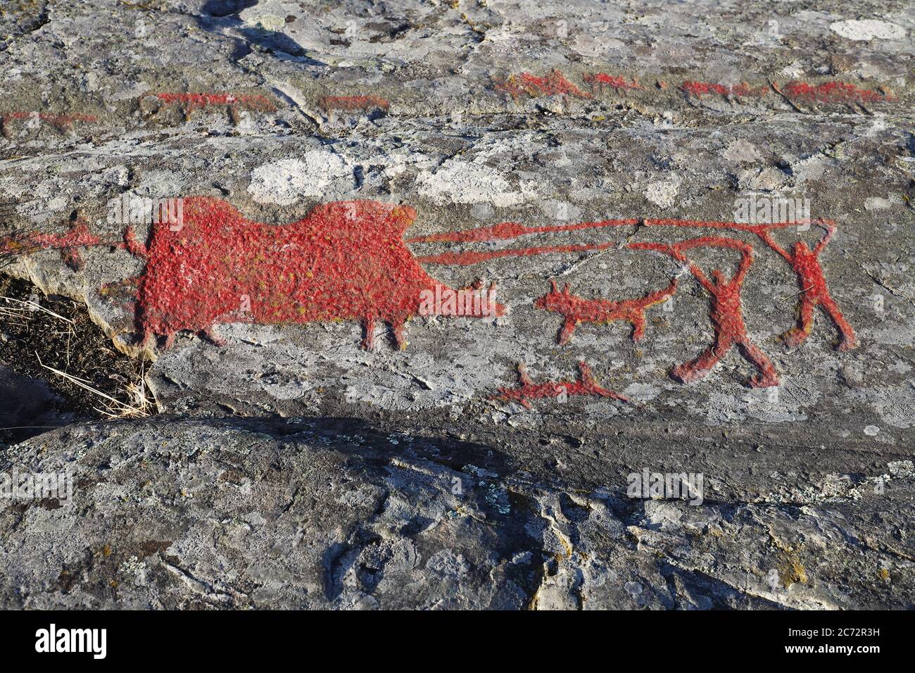 Felszeichnungen aus der Bronzezeit mit einer Szene, in der zwei Männer mit Hunden und Speeren ein riesiges Wildschwein jagen. Einer der Hunde ist tot. Die Schnitzereien sind Stockfoto