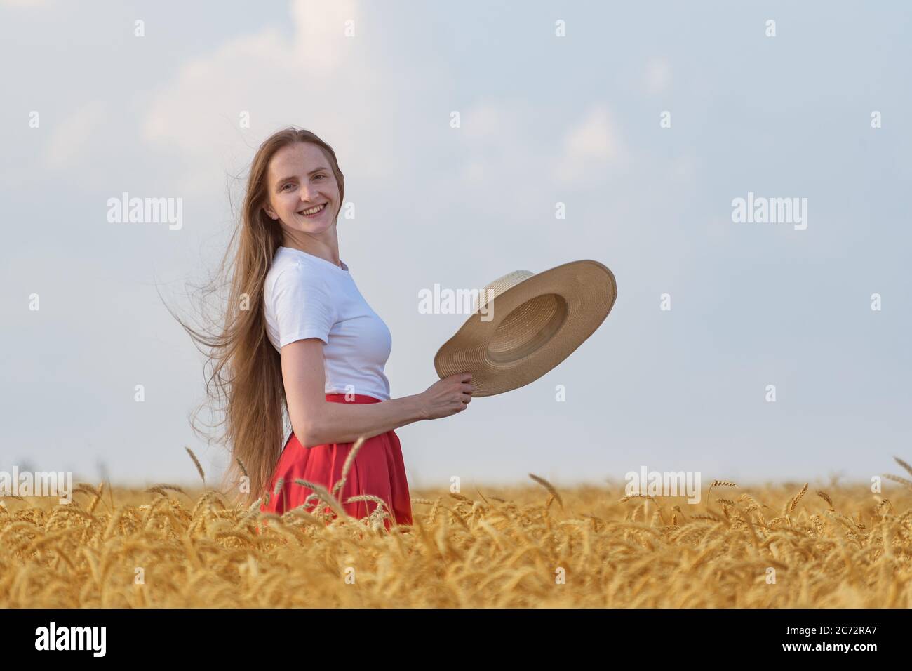 Junge Frau mit braunen Haaren steht im Feld von reifen Weizen hält Hut. Urlaub auf dem Land. Stockfoto