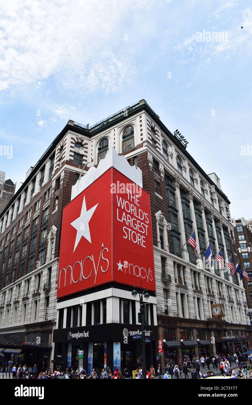 Die große rote Einkaufstasche bei Macy's, dem größten Kaufhaus der Welt in New York City. Amerikanische Flaggen hängen an der Seite des Ladens. Stockfoto