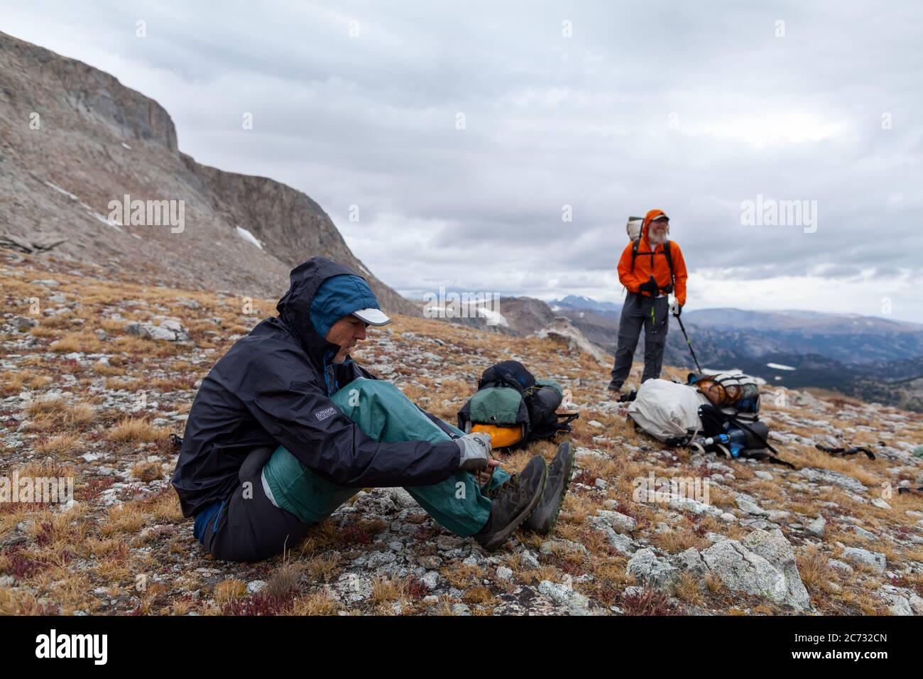 Ein männlicher Backpacker zieht Regenkleidung an, während stürmisches Wetter auf einem Sattel unterhalb des Europe Peak anrückt. Wind River Range, Wyoming Stockfoto