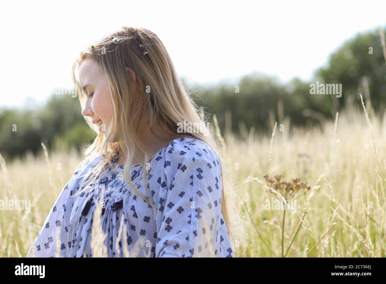 Ein junges hübsches Hippie-Mädchen mit blonden Haaren im Sonnenschein auf einem Weidefeld im Sommer. Stockfoto