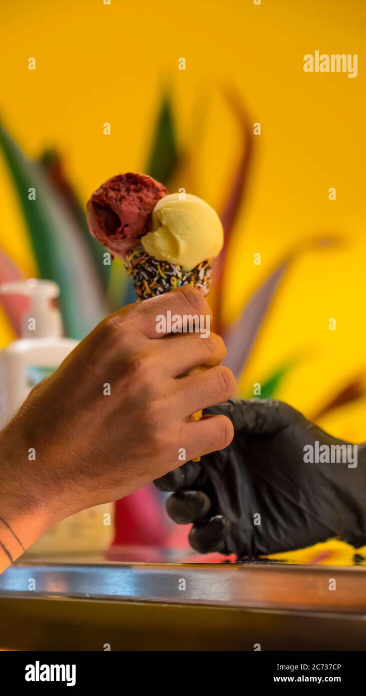 Verkäufer in Schürze hält Eis in einem Waffelkegel, Nahaufnahme. Verkauf von Eis in einem Geschäft Stockfoto