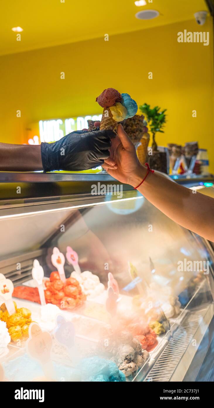 Verkäufer in Schürze hält Eis in einem Waffelkegel, Nahaufnahme. Verkauf von Eis in einem Geschäft Stockfoto