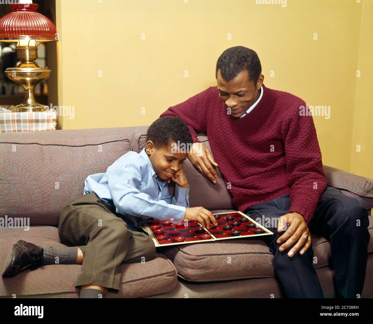 1960S 1970S AFRICAN AMERICAN VATER UND SOHN SITZEN AUF COUCH ZUSAMMEN IM WOHNZIMMER ZU HAUSE SPIELEN EIN SPIEL DER DAME - KJ5147 PHT001 HARS NOSTALGISCHE PAAR VORORT URBAN FARBE TEILEN ALTE ZEIT UNTERRICHT NOSTALGIE ALTE MODE 1 JUGENDLICH COUCH STIL KOMMUNIKATION WETTBEWERB SÖHNE FAMILIEN FREUDE LIFESTYLE ELTERNSCHAFT ZU HAUSE LEBEN COPY RAUM FREUNDSCHAFT HALBLÄNGE PERSONEN MÄNNER VÄTER DAME GLÜCK HIGH-ANGLE-STRATEGIE WOHNZIMMER AFROAMERIKANER AFROAMERIKANER UND VÄTER SLACKS SCHWARZE ETHNIZITÄT STOLZ AUF QUALITÄT VERBINDUNG PFLEGER BOARD SPIEL ZUSAMMENARBEIT JUGENDLICHE MITTE ERWACHSENE MITTE ERWACHSENE MANN Stockfoto