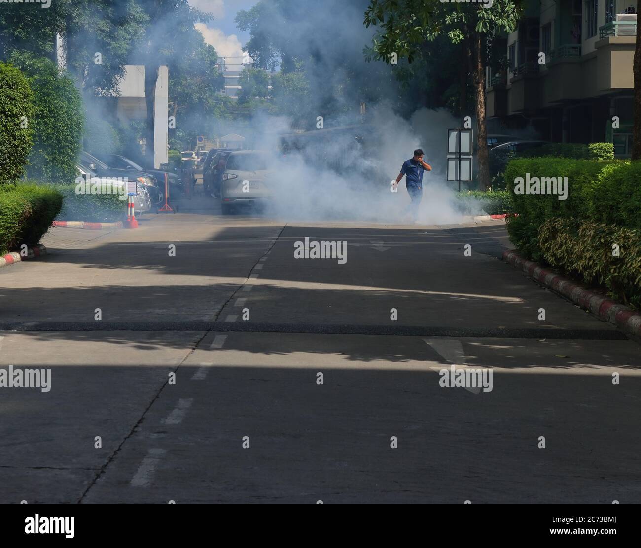 Bangkok, Thailand - 13. Juli 2020: Ein Arbeiter, der mit der Hand durch Rauch läuft, der durch das Spritzen von Insektizid um die Gebäude verursacht wird Stockfoto