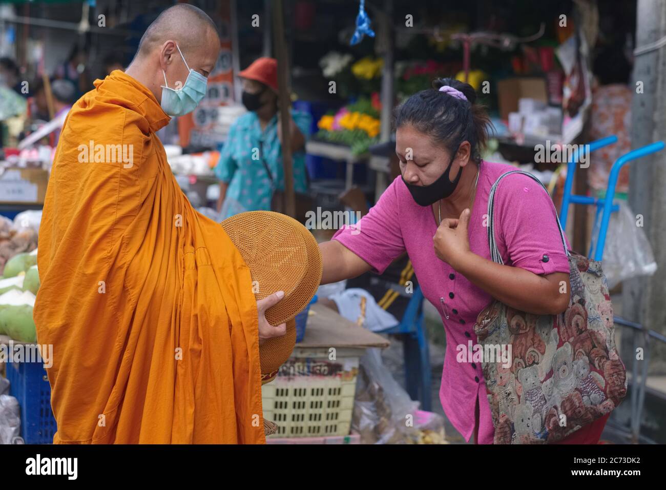 Ein buddhistischer Mönch auf seiner Morgenalmosenrunde (binta baat) und mit Almosenschale (baat) wird von einer Laienfrau, Phuket Thailand, Almosen gegeben Stockfoto