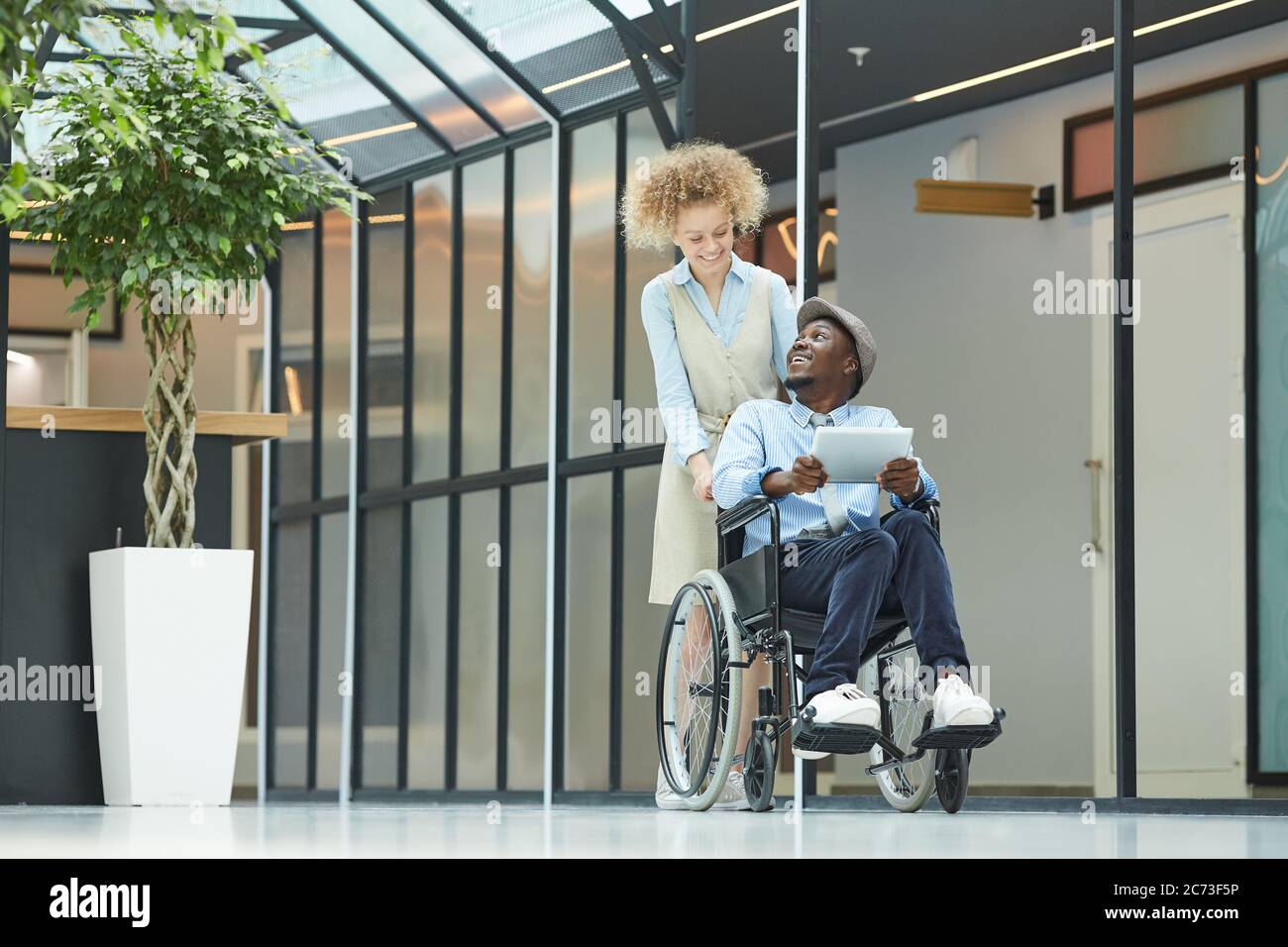 Junge Frau, die den Flur mit behinderten Mann im Rollstuhl er mit Tablet-pc Stockfoto