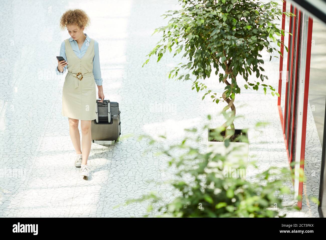 Junge Geschäftsfrau, die mit Koffer und Handy den Bürogang entlang läuft Stockfoto