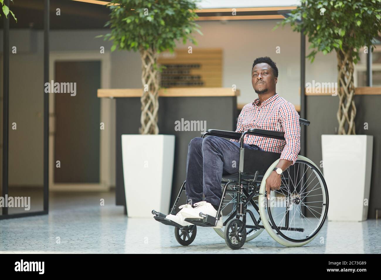 Afrikanischer behinderter Geschäftsmann sitzt im Rollstuhl, er arbeitet im Bürogebäude Stockfoto