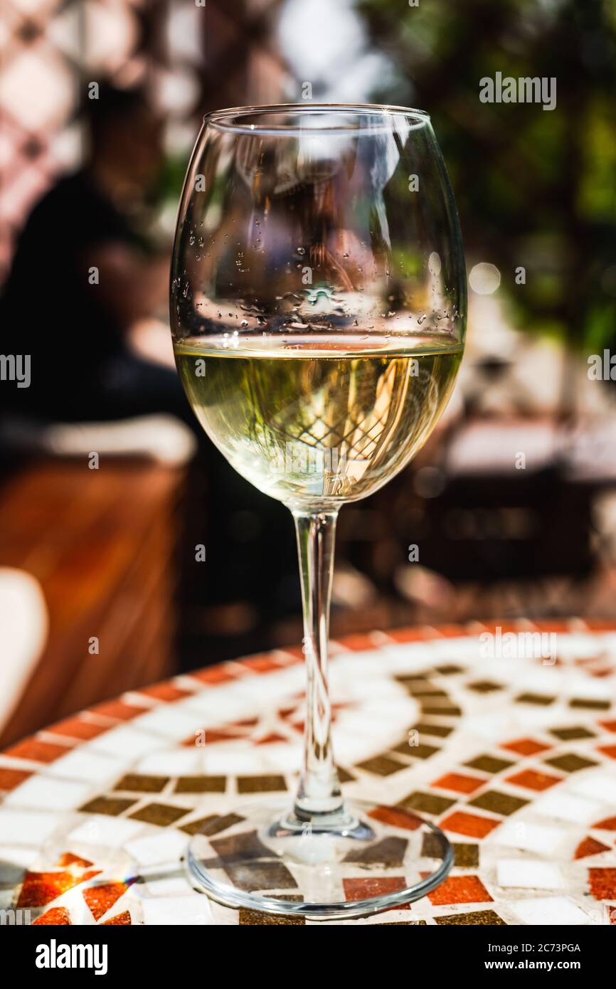 Ein Glas Weißwein auf einem Mosaiksteintisch einer Café-Terrasse an einem sonnigen Tag Stockfoto