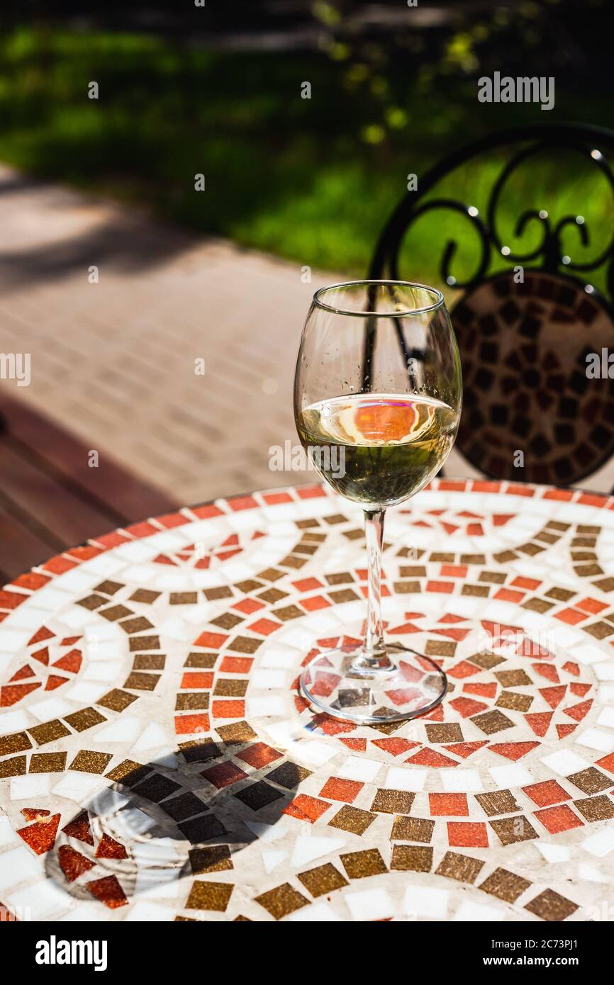 Ein Glas Weißwein auf einem Mosaiksteintisch einer Café-Terrasse an einem sonnigen Tag Stockfoto