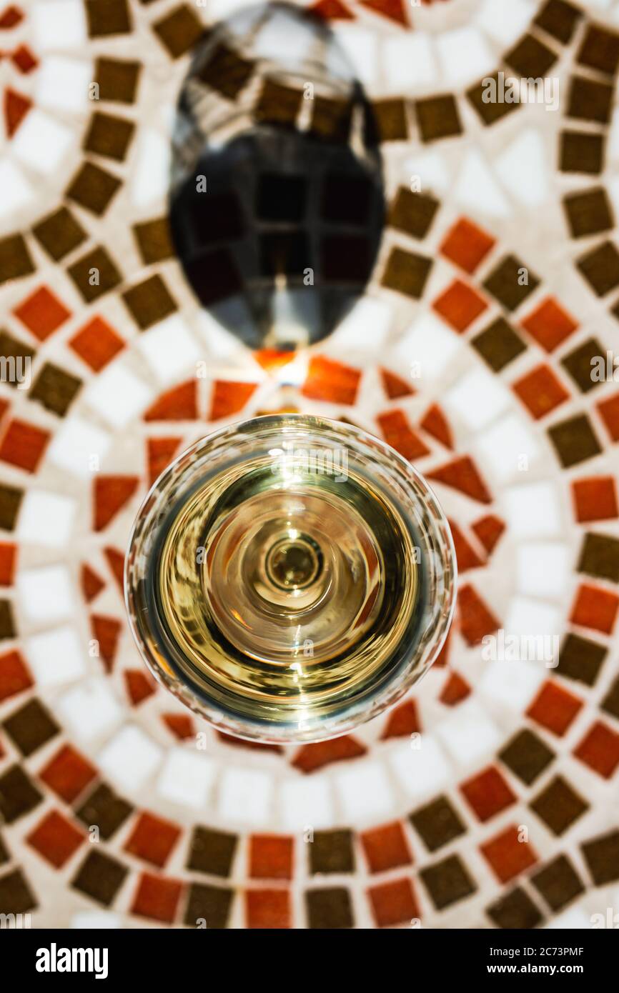 Ein Glas Weißwein auf einem Mosaiksteintisch einer Café-Terrasse an einem sonnigen Tag, Blick von oben Stockfoto