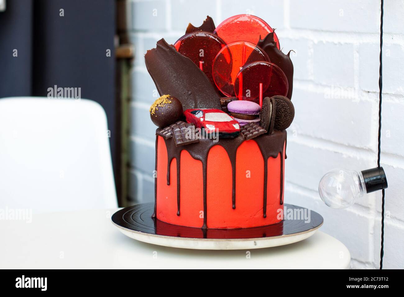 Roter Kuchen mit Schokolade Rennwagen, Schokolade Dekoration, Makronen, Lutscher und Cookies. Weißer Hintergrund. Stockfoto