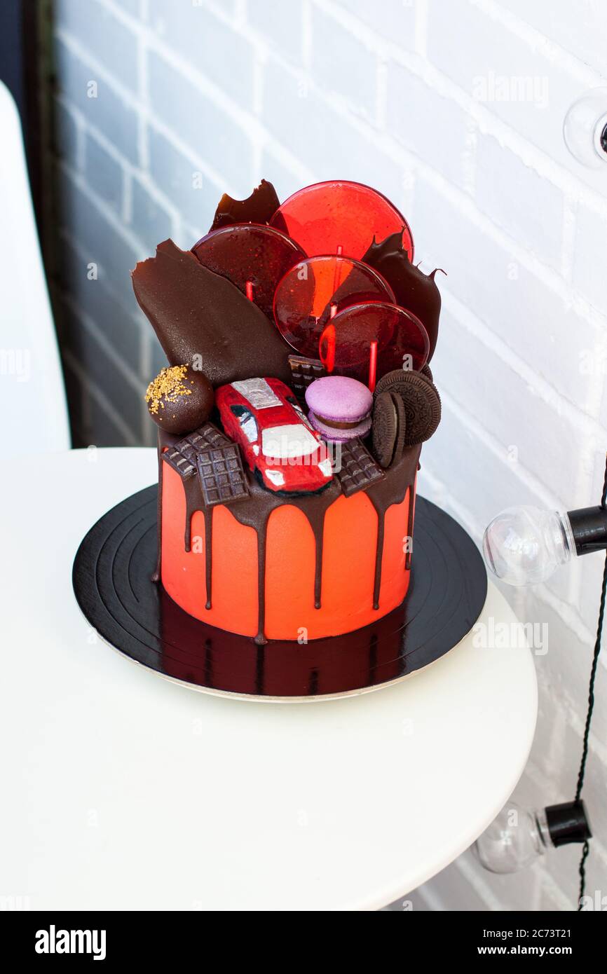 Roter Kuchen mit Schokolade Rennwagen, Schokolade Dekoration, Makronen, Lutscher und Cookies. Weißer Hintergrund. Stockfoto