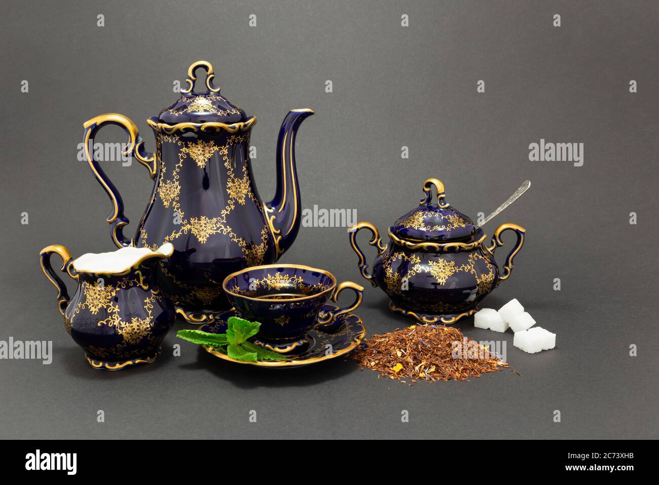 Stillleben mit einem kobaltblauen Vintage Porzellan Teeset, Löffel mit Zuckerwürfeln, Zuckerdose, Milchkrug und trockenen Teeblättern. Stockfoto