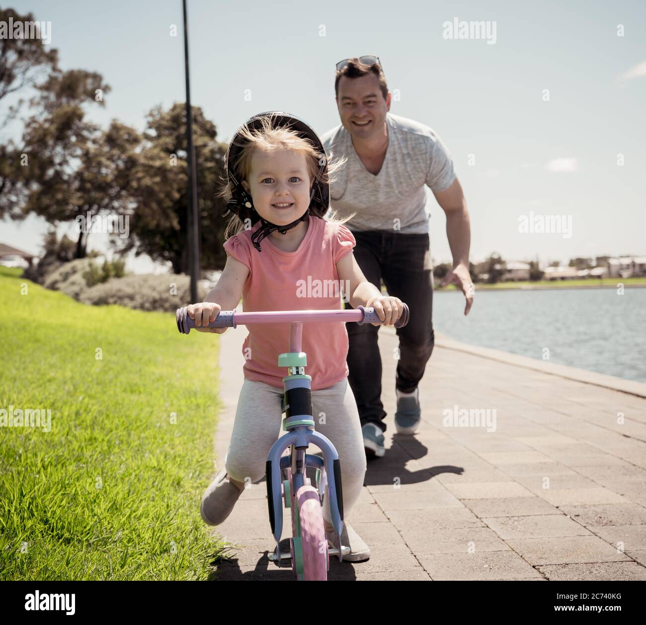 Kleines Mädchen lernen, ein Fahrrad mit seinem Vater im Park am See zu fahren. Vater und Tochter verbinden und Spaß zusammen haben. Glückliche Familie, out Stockfoto