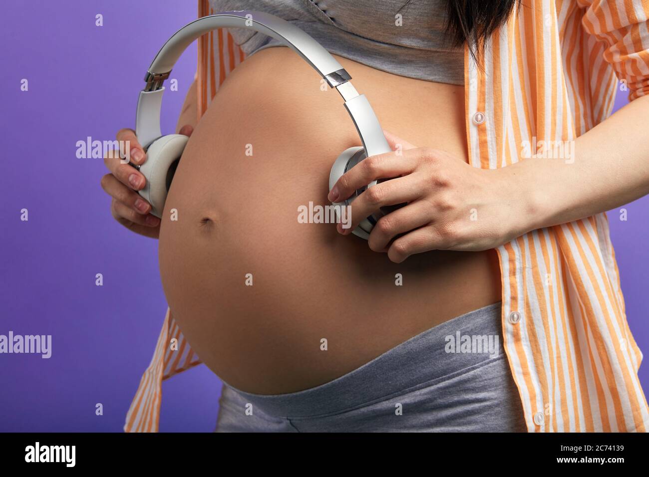 Zukünftige Mutter hält Kopfhörer auf ihrem großen Bauch, während ihr ungeborenes Baby angenehme Klänge und Melodie hört. Vorfreude Auf Das Erste Kind Stockfoto