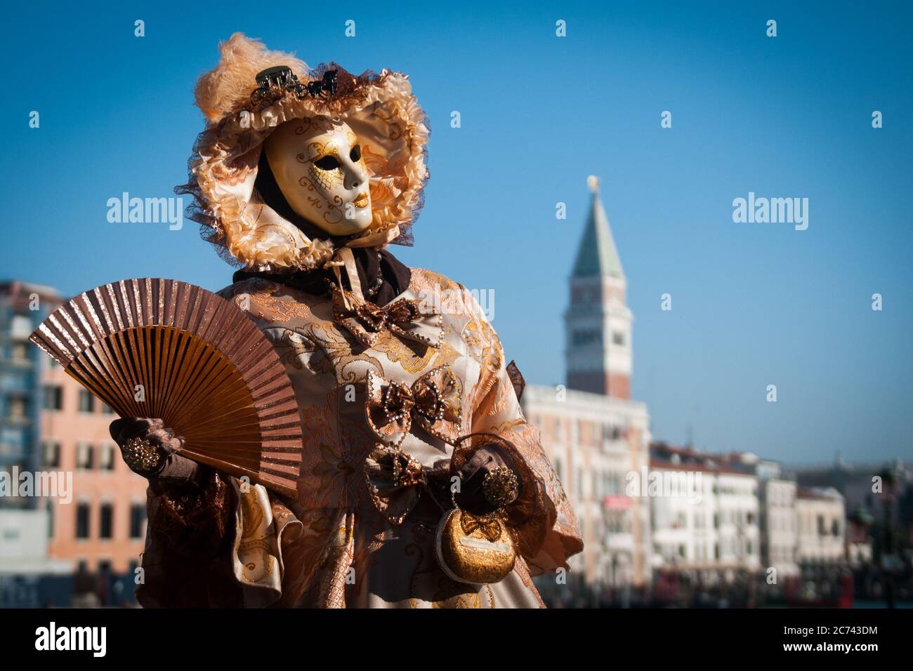 VENEDIG, ITALIEN - 28. FEBRUAR 2020: Eine goldene Maske während des Karnevals in Venedig winkt einem Fächer mit dem Markusplatz im Hintergrund Stockfoto