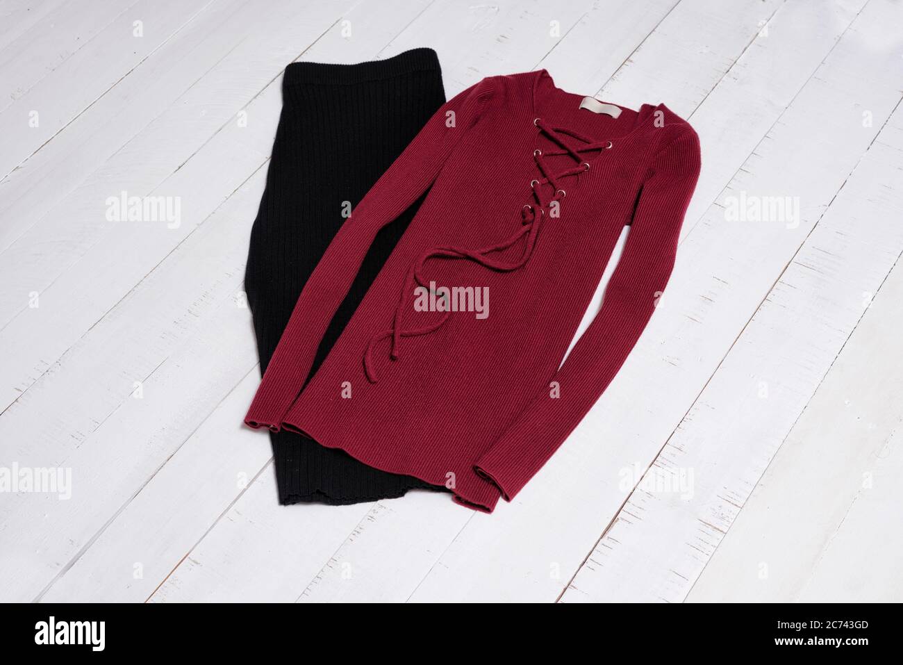 Kleidung und Accessoires. Schwarzer Midi-Rock und roter Pullover mit Schnürung auf weißen Holzbodenteelen. Flach liegend. Stockfoto