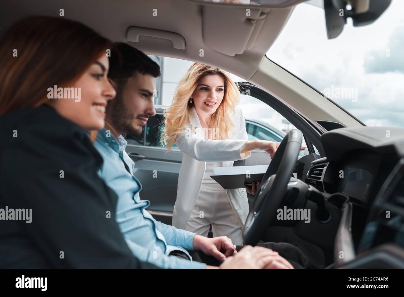 Junges Paar im Auto. Eine Beraterin zeigt einem jungen Paar ein Auto. Junge Familie wählt Auto bei einem Autohaus Stockfoto
