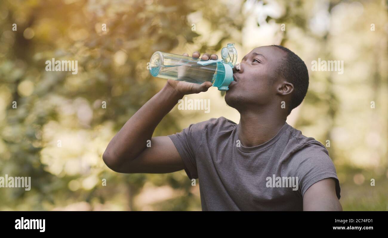 Junger schwarzer Mann, der Wasser aus der Sportflasche im Park trinkt Stockfoto