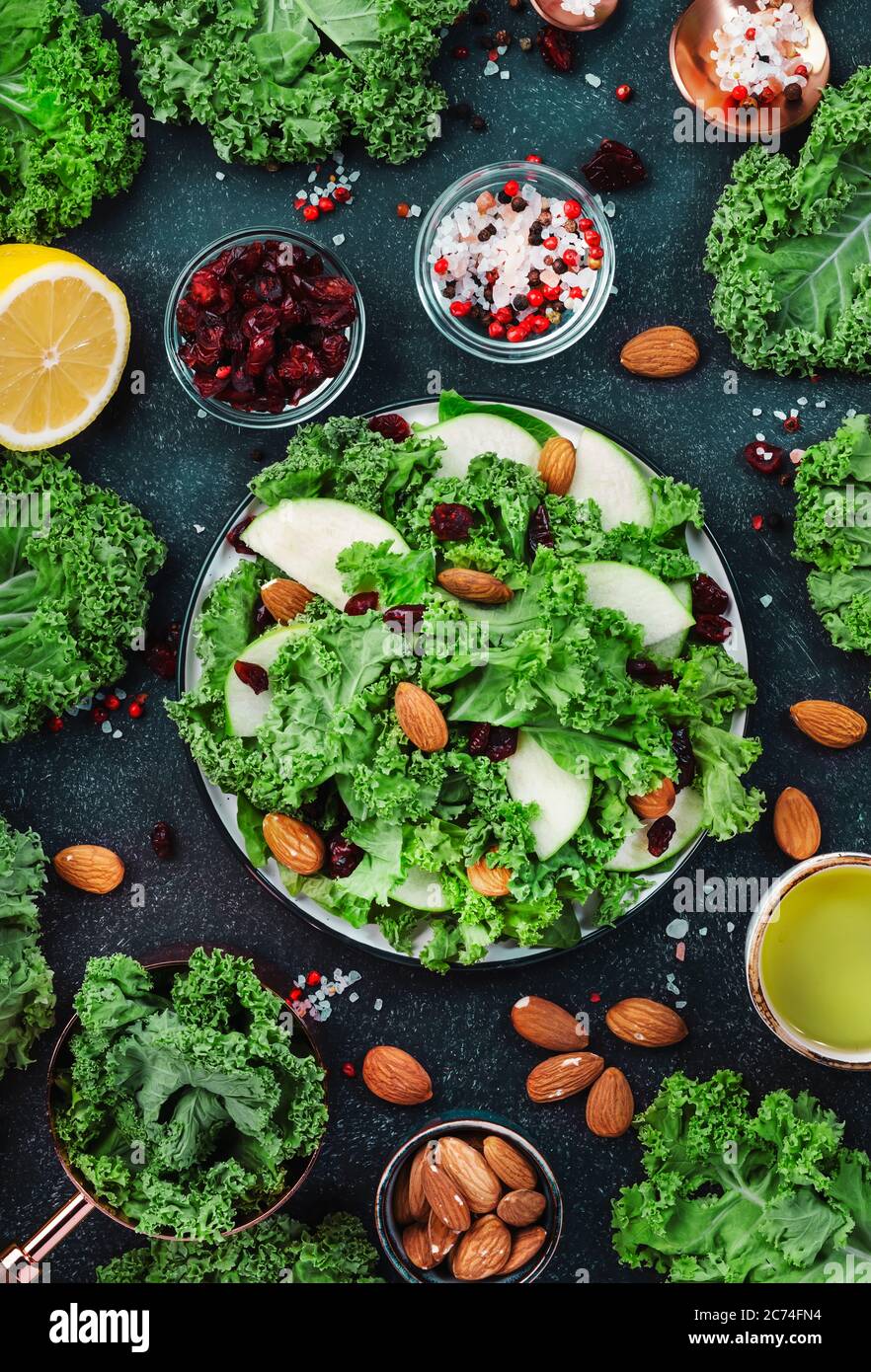 Kalesalat mit getrockneten Preiselbeeren, grünen Äpfeln und Mandeln. Gesundes veganes Essen, Draufsicht, schwarzer Küchentisch Hintergrund Stockfoto
