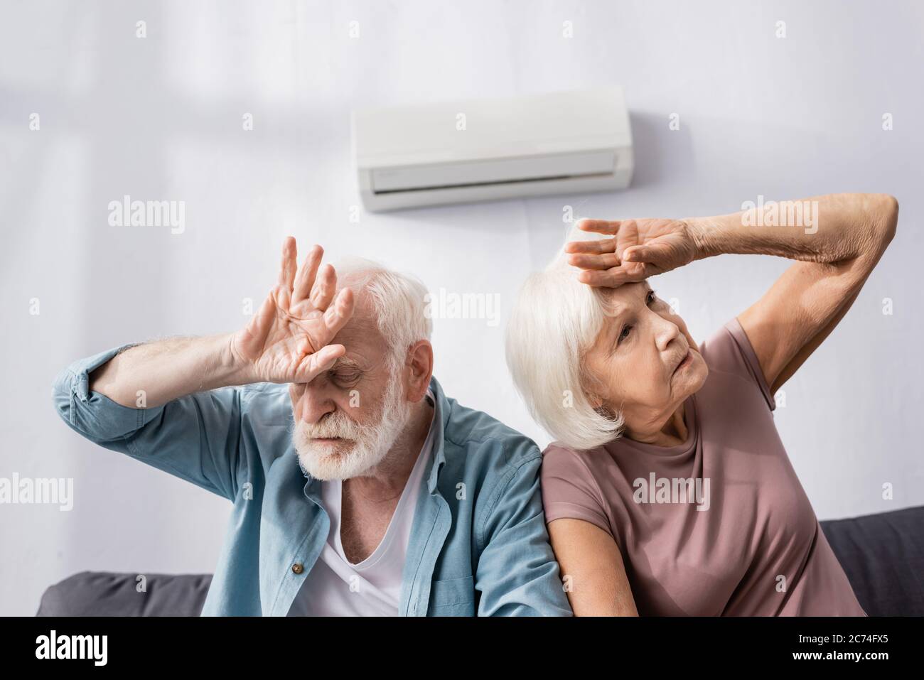 Ältere Paare leiden unter Hitze, während sie unter Klimaanlage zu Hause sitzen Stockfoto