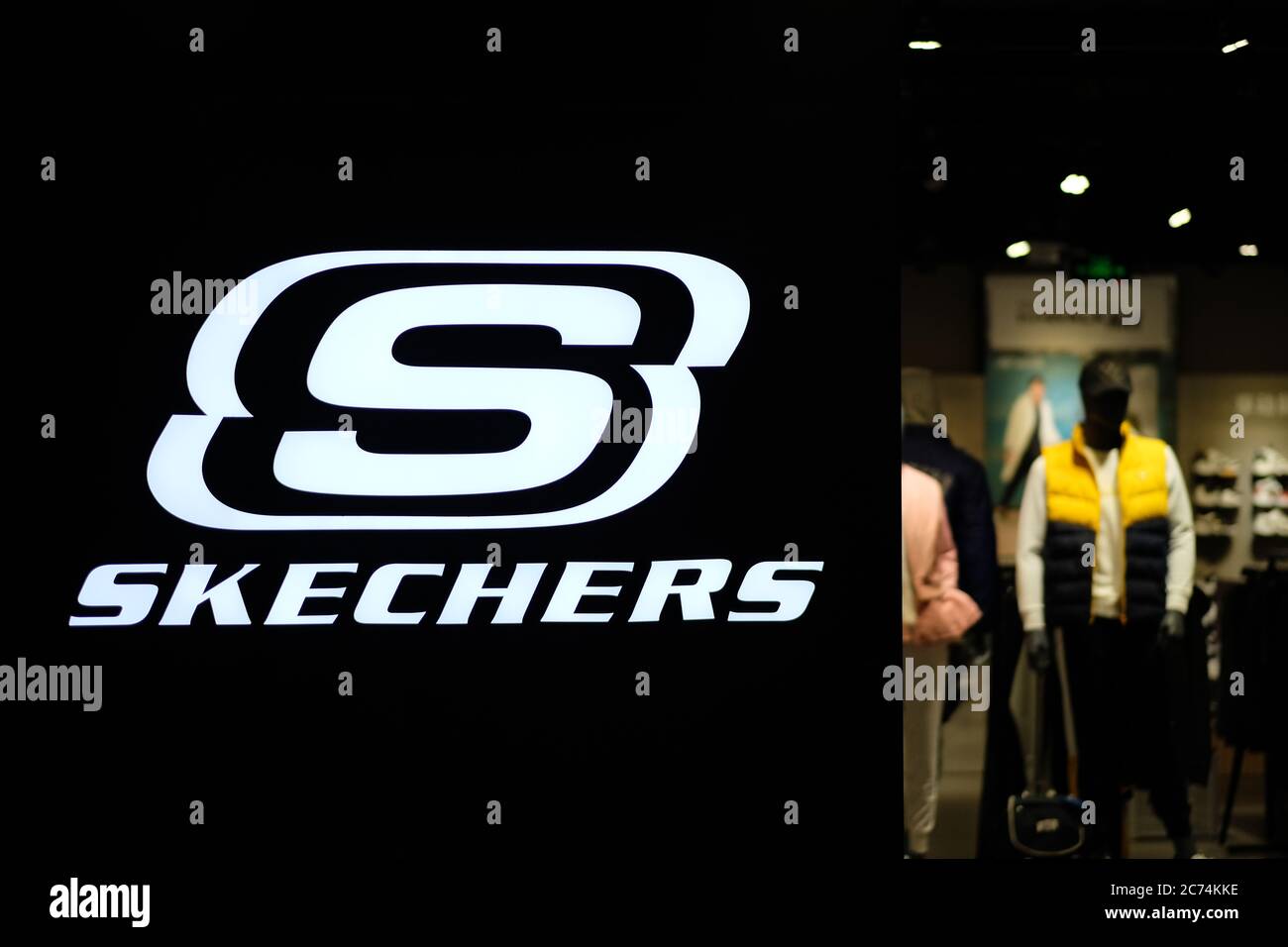 Nahaufnahme strahlend weißes SKECHERS-Logo an der schwarzen Außenwand des Geschäfts. Verwischen Sie Kleidung als Hintergrund. Eine berühmte Marke von Schuhen Stockfoto