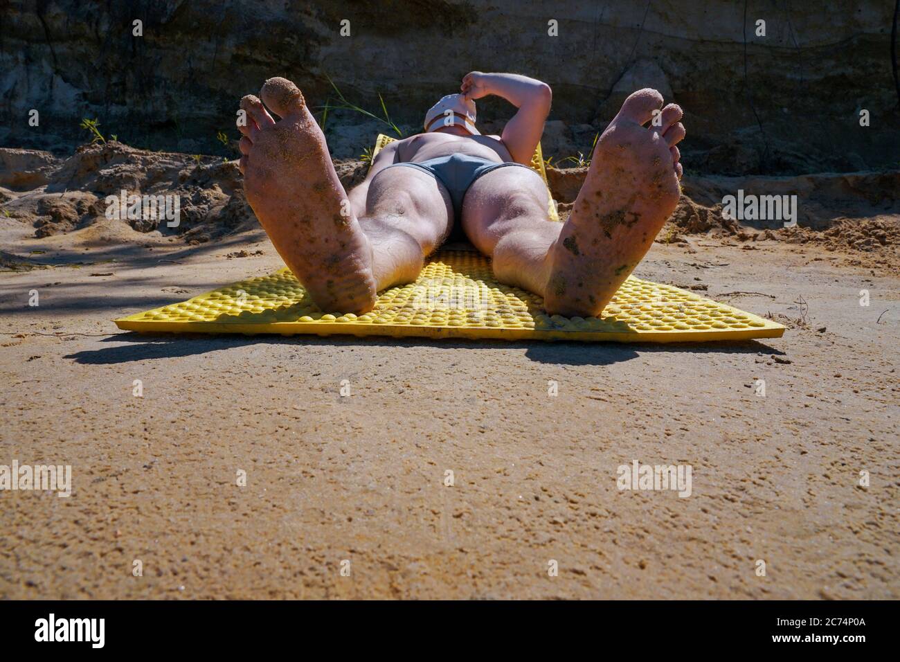 Der Typ im Hut und Badehose liegt am Ufer und sonnen sich unter der Sonne auf der Insel Stockfoto