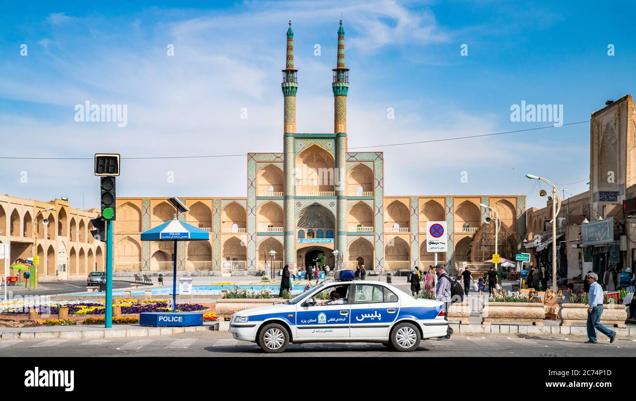 Yazd, Iran - Mai 2019: Tore und Minarette der Jameh Moschee von Yazd mit einem Polizeiauto und Menschen während des Stadtlebens Stockfoto