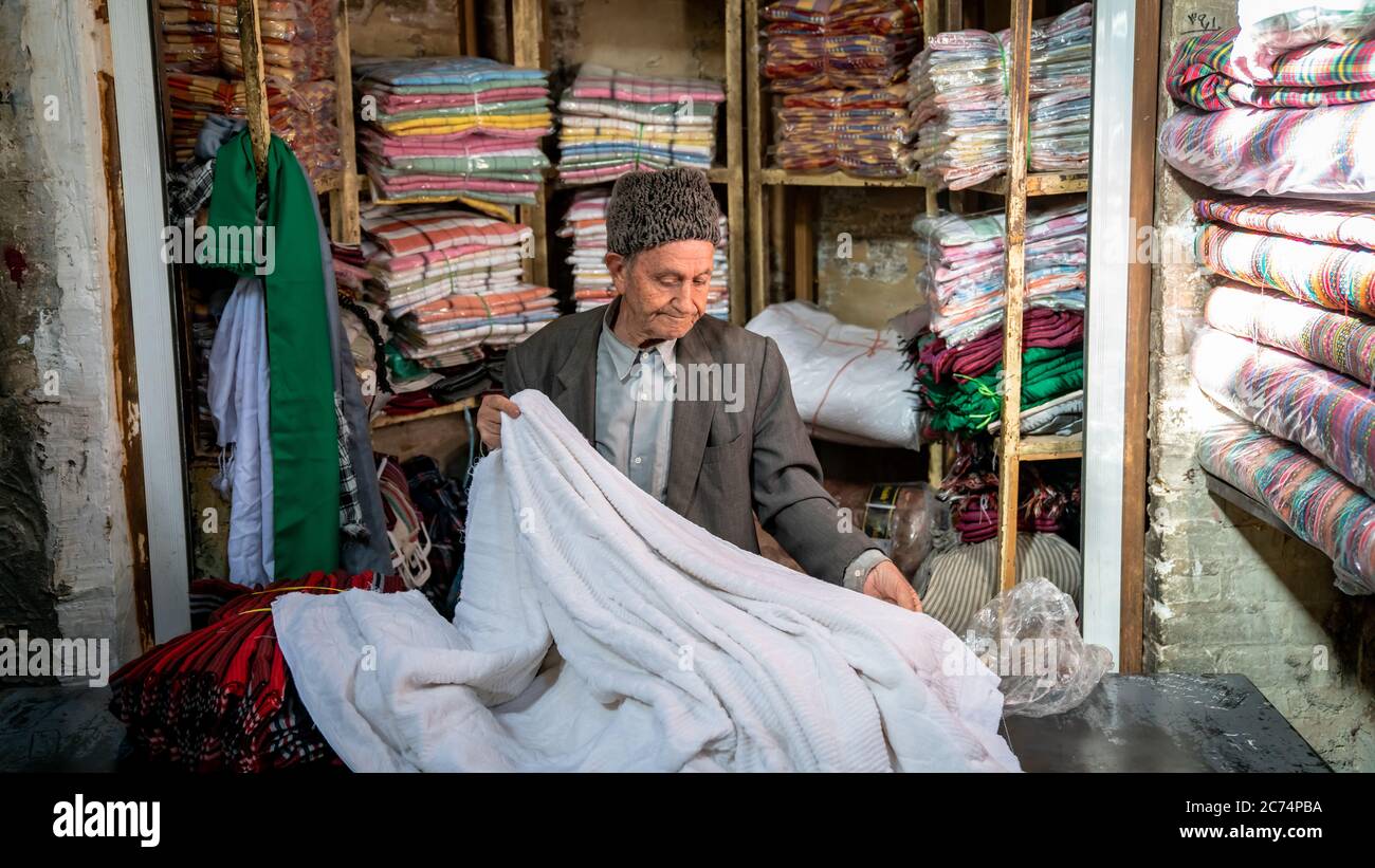 Isfahan, Iran - Mai 2019: Der alte iranische Mann verkauft in seinem kleinen Laden im Großen Basar von Isfahan Textilien Stockfoto