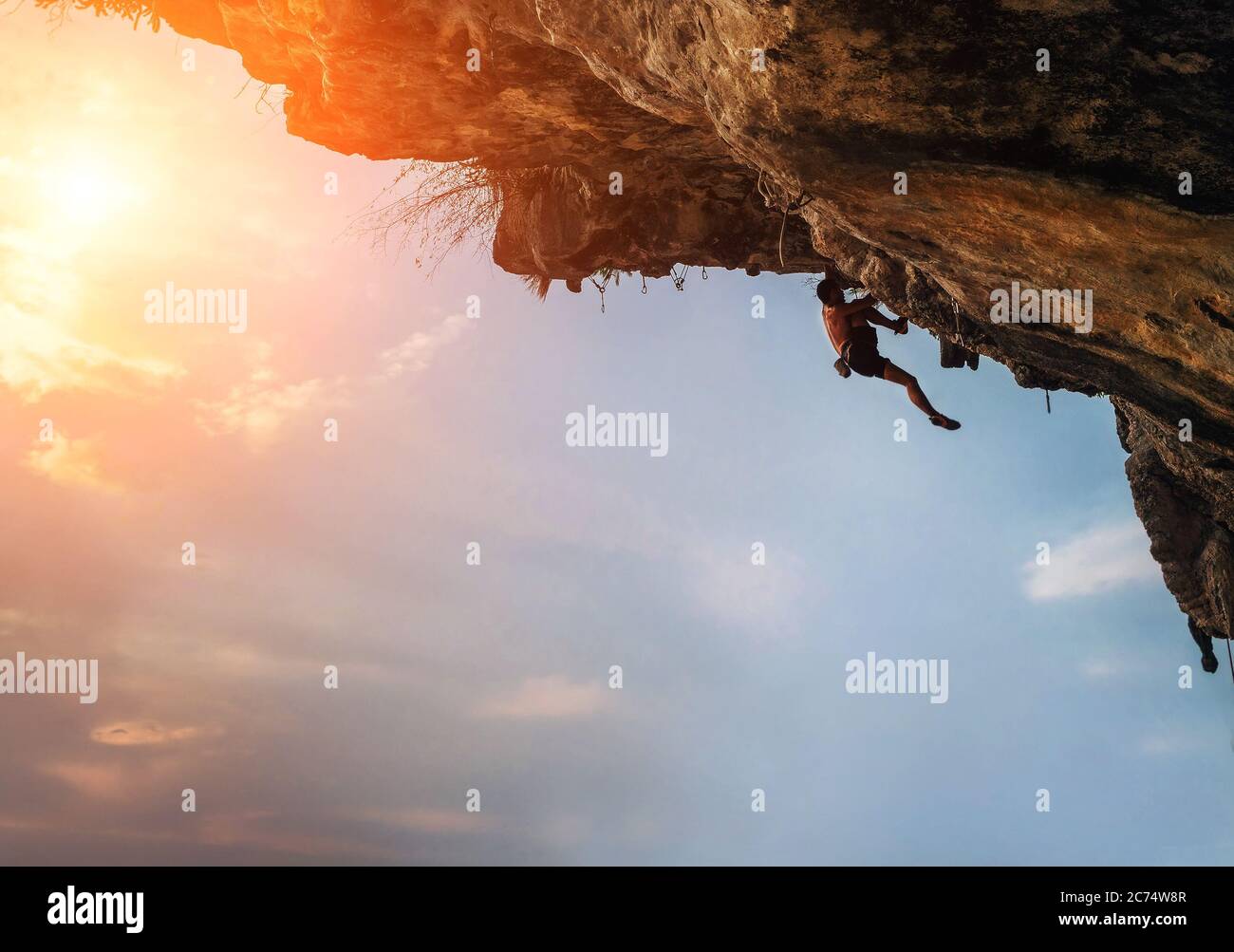 Athletic man Klettern auf überhängenden Felsen mit bunten Sonnenuntergang Himmel Hintergrund Stockfoto