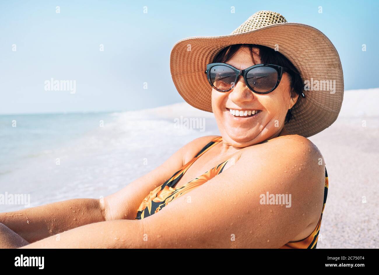 Glücklich lächelnde ältere Frau in Sonnenbrille und großen Hut nehmen Sonnenbad auf dem Seeseite Porträt Stockfoto