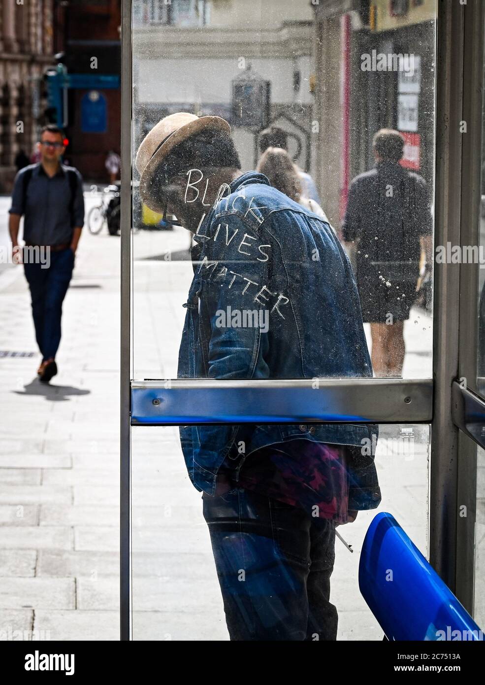 Schwarzer Mann wartet an einer Bushaltestelle in Brighton, wo Black Lives Matter an das Glas gekratzt ist Stockfoto