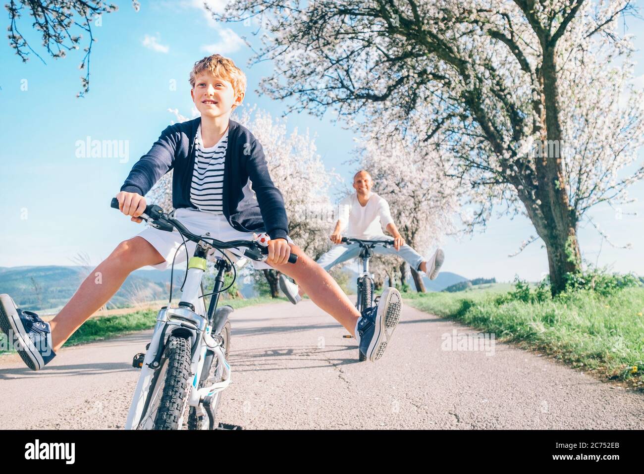 Vater und Sohn haben Spaß, breiten Beinen beim Radfahren auf Landstraße unter Blütenbäumen zu verbreiten. Gesundes sportliches Lifestyle-Konzept. Stockfoto