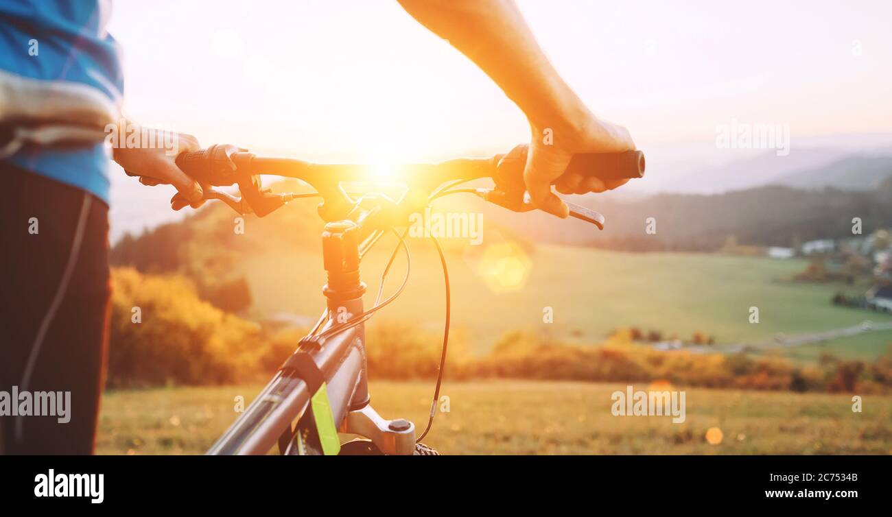 Mann mit Fahrrad bleibt auf einem Hügel und genießt den Sonnenuntergang. Mann Hände auf dem Fahrrad Lenkrad Nahaufnahme Bild Stockfoto