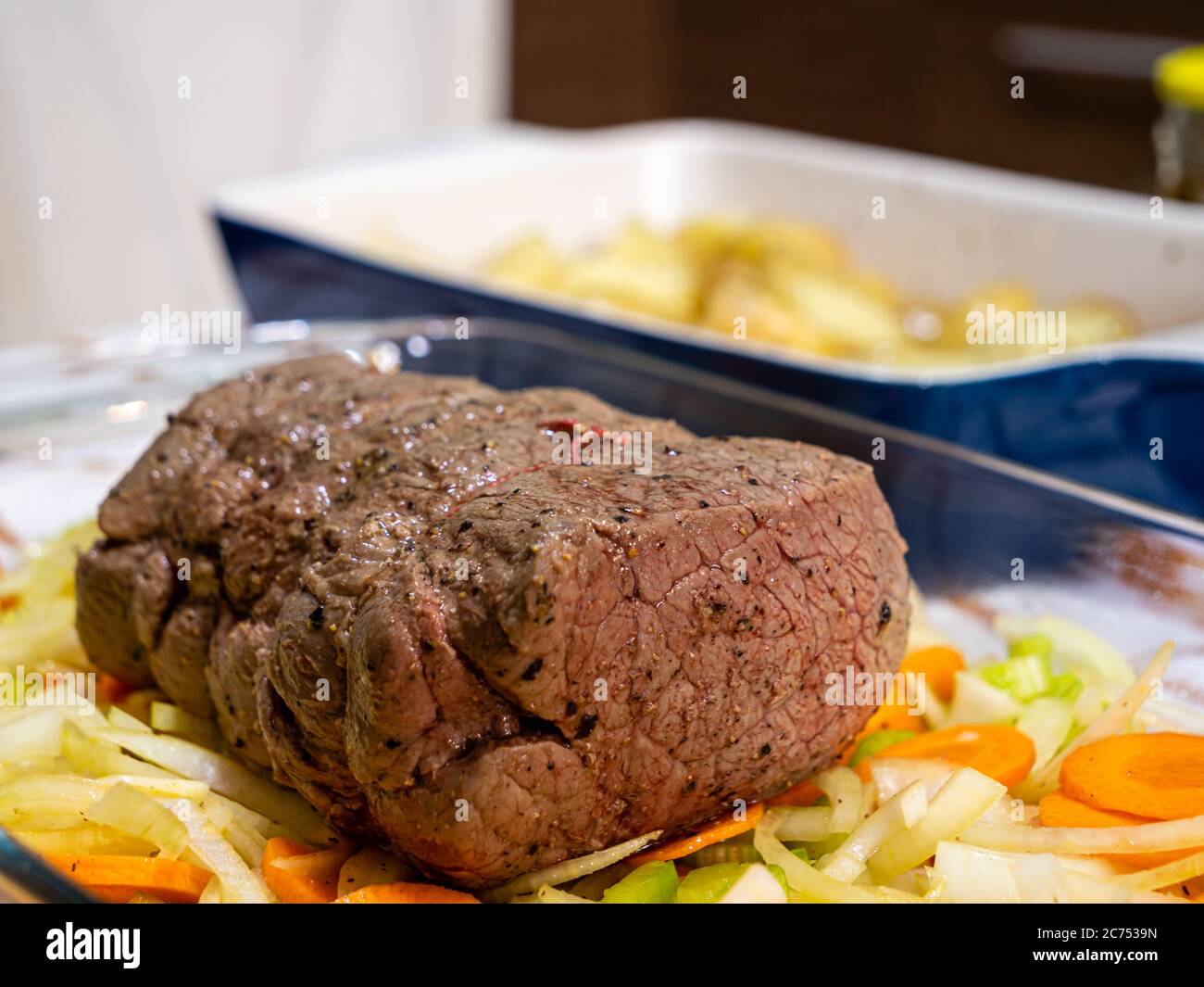 Ein traditionelles Sonntagsbraten mit einem Rinderbraten und Kartoffeln auf einer rustikalen karierten Tischdecke in einer heimischen Küche Stockfoto