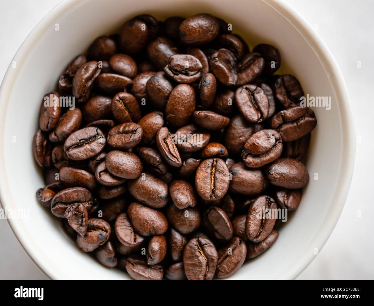 Makro-Nahaufnahme von gerösteten Kaffeebohnen in einer weißen Tasse vor weißem Hintergrund Stockfoto