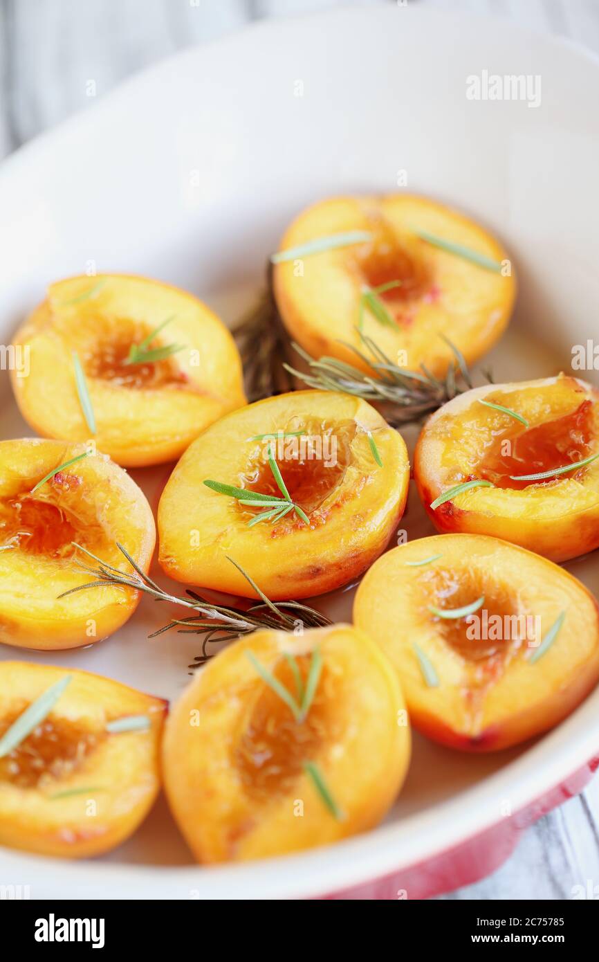 Frisch gebackene, hausgemachte Pfirsiche in braunem Zucker und frischen Rosmarinzweigen gebacken. Selektiver Fokus mit unscharfem Vorder- und Hintergrund. Stockfoto