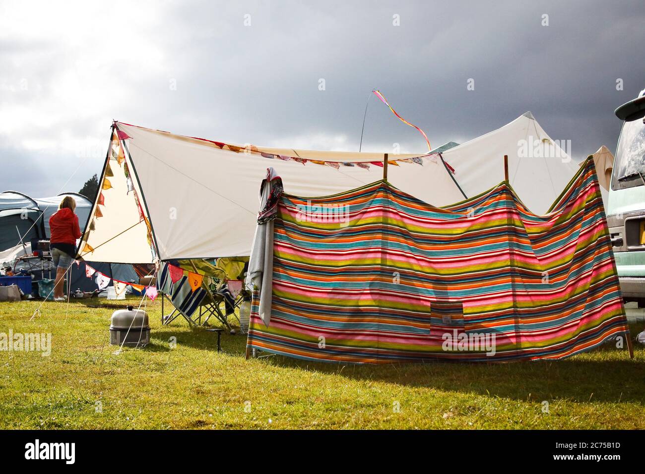 Bunte stripey Camping Windbreak und Markise für Schatten mit Ammern und dunklen Sturm regen Wolken auf einem Festival-Campingplatz in Norfolk. Stockfoto