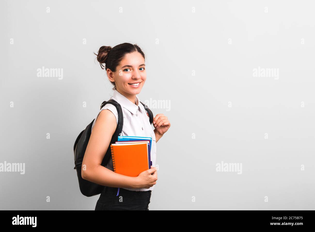 Attraktive Studentin mit Grübchen in Wangen lächelnd hält Notizbücher in einer Hand und Rucksack auf Schultern mit niedlichen Gesichtsausdruck Stockfoto