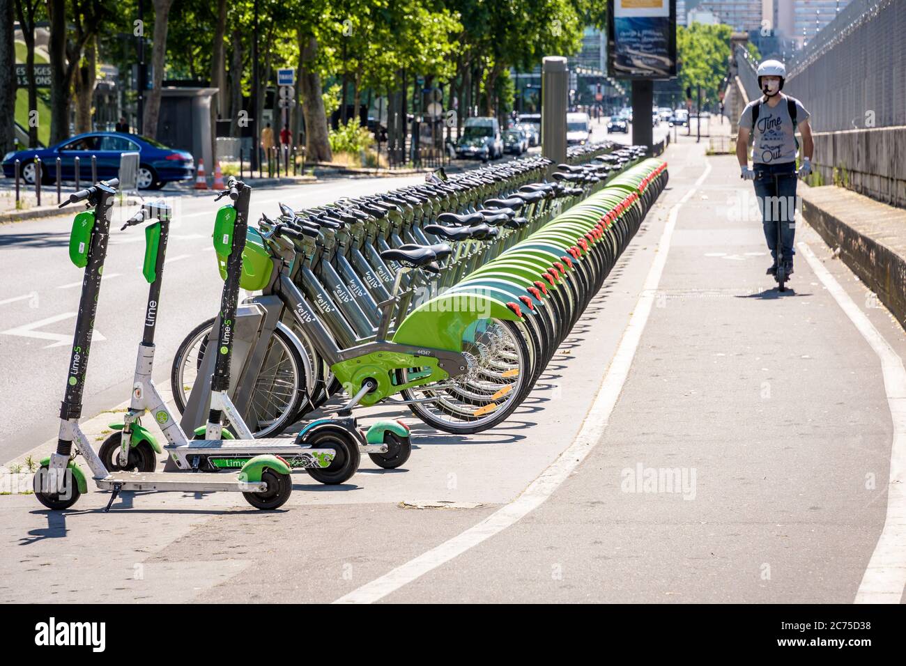 Ein Mann, der einen Elektroroller auf einer Fahrradspur an einer Reihe Velib vorbei fährt, teilte Fahrräder, die an einer Station zusammen mit Lime Elektrorollern in Paris geparkt waren. Stockfoto