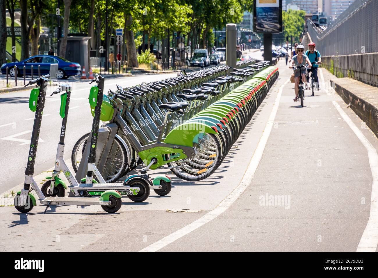 Fahrradfahrer, die auf einer Fahrradstraße an einer Flotte von Velib-Fahrrädern vorbeifahren, Reihen sich an einer Anlegestelle zusammen mit Lime-Elektrorollern in Paris an. Stockfoto