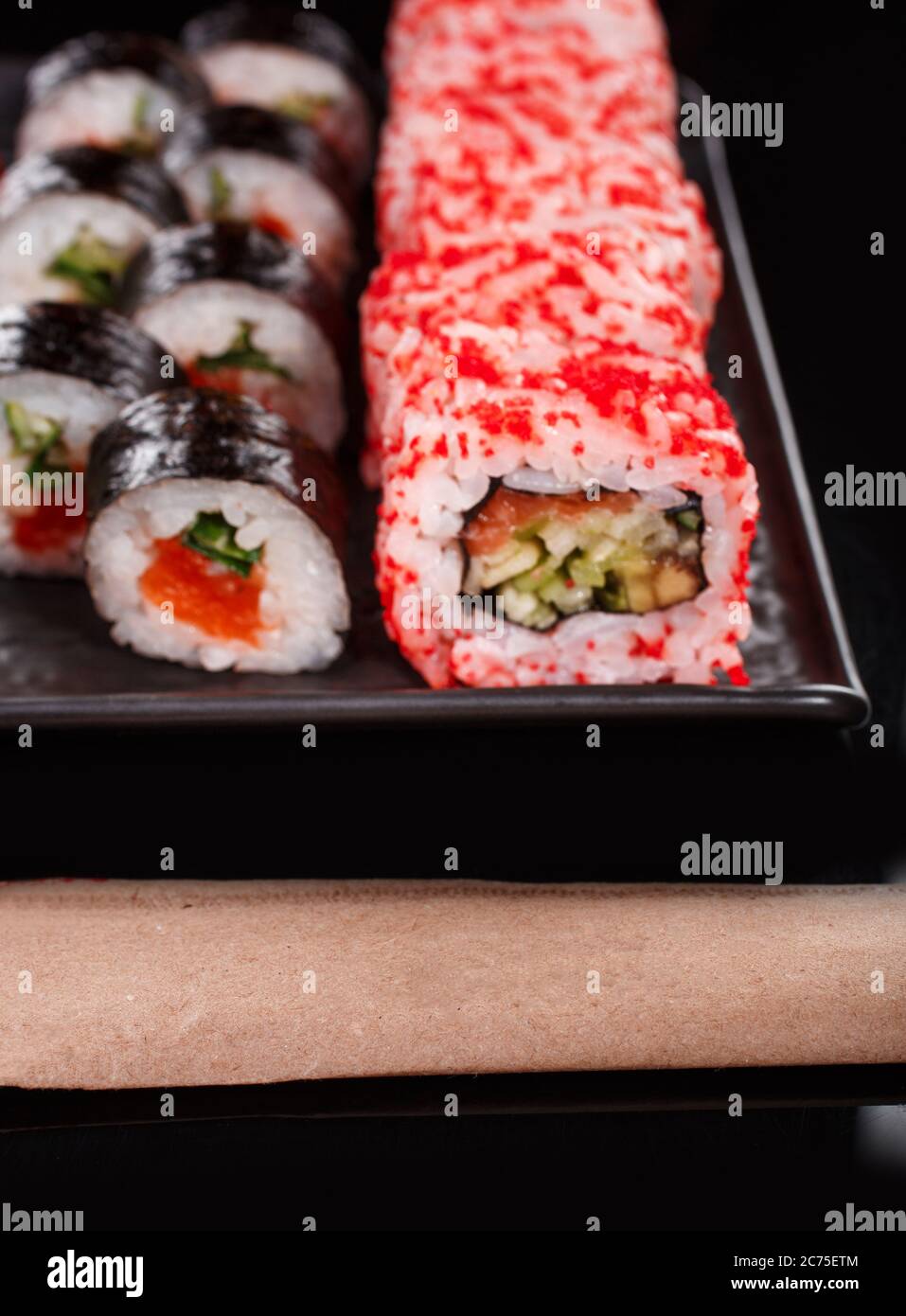 Sushi-Set aus Uramaki und Maki mit rotem Kaviar, Lachs und Gurke. Serviert auf einem schwarzen Teller. Stockfoto