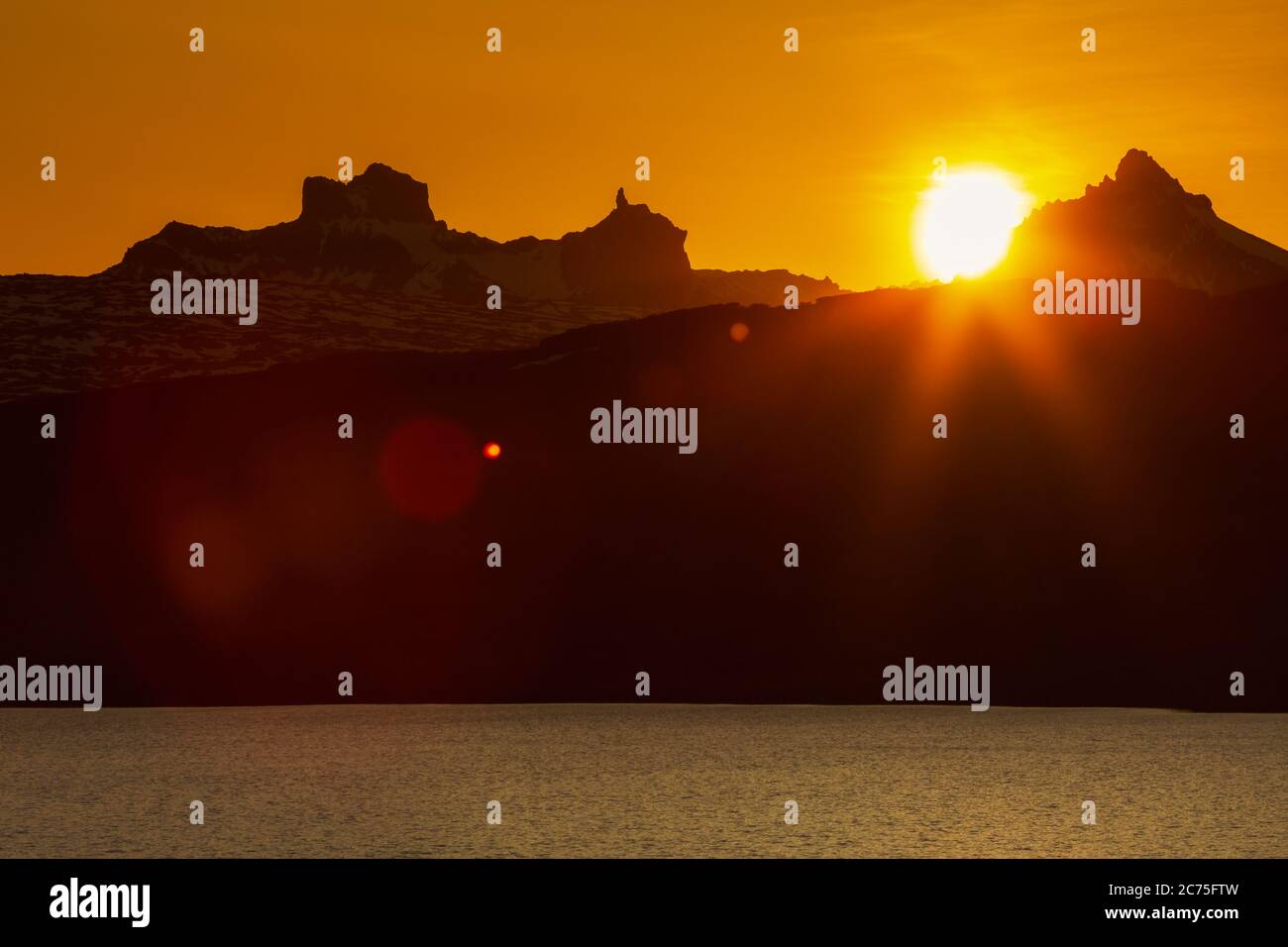 Schöner Sonnenuntergang in felsigen Bergen und Seeufer, rot orange Sonne untergeht hinter Silhouette der Klippe Bergkette, malerische Landschaft Stockfoto
