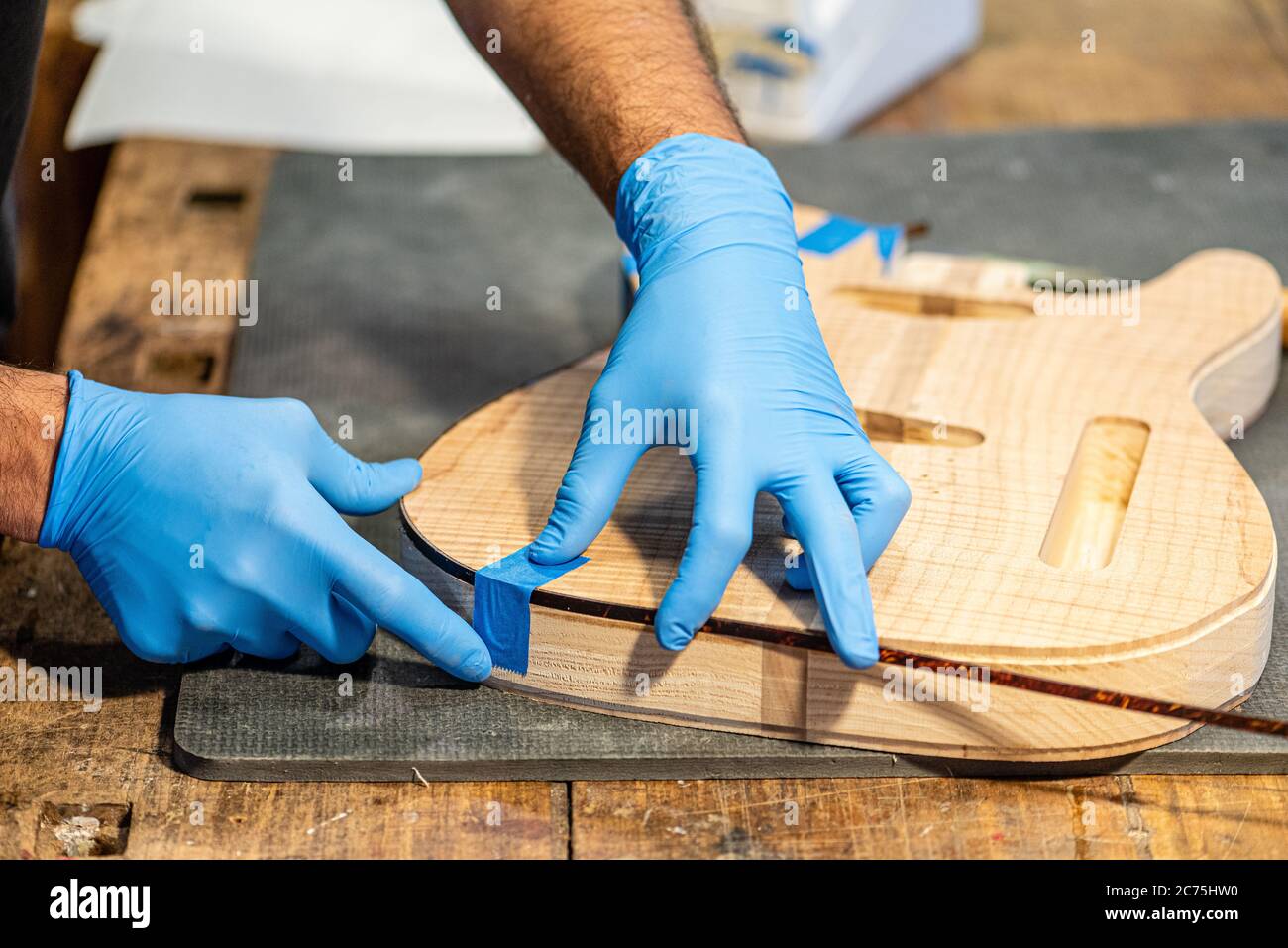 Nahaufnahme der Hände eines Geigenbauers bei der Arbeit am Körper einer Gitarre, Hände eines Handwerkers mit Schutzhandschuhen, Musikgeschäft und Bau von Musical Stockfoto